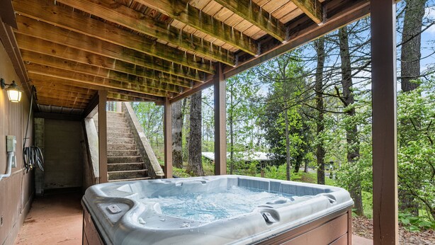 A hot tub under a wooden pergola with a staircase leading to an upper level.