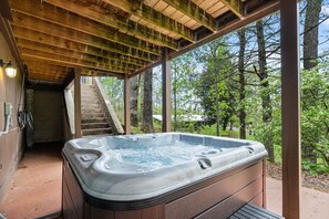 A hot tub under a wooden pergola with a staircase leading to an upper level.