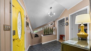 A hallway with a yellow door, a ceiling fan, a glass-top table with a lamp, and a plant shelf.