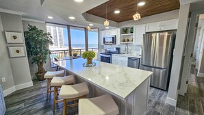 A modern kitchen with a large island, stainless steel appliances, and a view of the ocean. - Superbly Updated Ocean View Condo, 303 Brighton, Full Access 3 Bedroom Condo (Myrtle Beach)