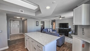 A spacious kitchen with a central island, a dining area with a dark wood table, and a living room with a blue sofa. - 1707 Brighton, impressively remodeled, 3 bedroom ocean view 3 Condo (Myrtle Beach)