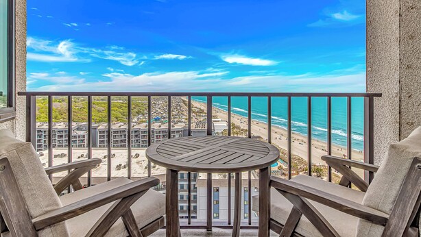 A balcony with a table and two chairs, overlooking a beach and ocean. - Myrtle Beach Resort RT1205 (Myrtle Beach)