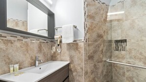 A modern bathroom with a vanity, a mirror, a towel rack, and a shower area. - Right Direction Rentals Studio Villa 8419 (Port St. Lucie)