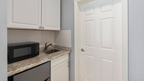 A kitchen with white cabinets, a granite countertop, a black microwave, and a stainless steel sink. - Right Direction Rentals Studio Villa 8419 (Port St. Lucie)