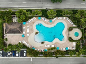 An aerial view of a resort with a large irregularly shaped swimming pool, lounge areas with sunbeds, and a small circular hot tub. - Right Direction Rentals Studio Villa 8419 (Port St. Lucie)