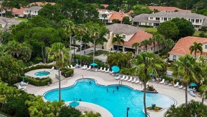 A large swimming pool surrounded by palm trees and lounge chairs, with houses in the background. - Right Direction Rentals Studio Villa 8419 (Port St. Lucie)