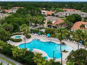 A large swimming pool surrounded by palm trees and lounge chairs, with houses in the background. - Right Direction Rentals Studio Villa 8419 (Port St. Lucie)