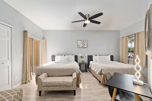 A hotel room with two beds, a ceiling fan, a desk with a lamp, and a view of the outside. - Right Direction Rentals Studio Villa 8419 (Port St. Lucie)