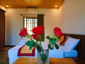 A hotel room with a bed, a wooden table, and a vase with red roses. - Valentina Resort & Spa (Phu Quoc)