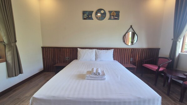 A hotel room with a large bed, a wooden headboard, a bedside table, a chair, a mirror, and artwork on the wall. - Valentina Resort & Spa (Phu Quoc)