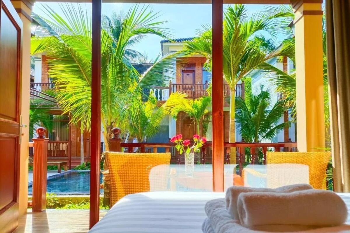 A hotel room with a bed, a view of a pool, and palm trees.