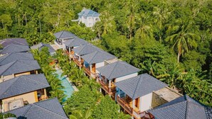 Un resort con varias edificaciones tipo bungalow, una piscina central y exuberantes jardines tropicales.