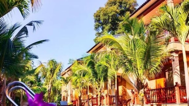 Un resort con piscina que refleja palmeras y un edificio con balcones.