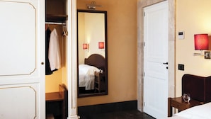 A hotel room with a wardrobe, a bed, a bedside table, a mirror, and a wall-mounted lamp. - Locanda Gulfi (Chiaramonte Gulfi)