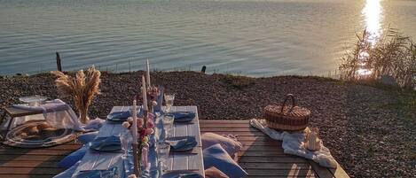 A wooden deck with a table set for a meal, overlooking a calm body of water.