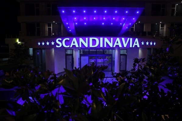 Un hôtel appelé « SCANDINAVIE », doté d’une façade moderne et d’une enseigne lumineuse bien visible.