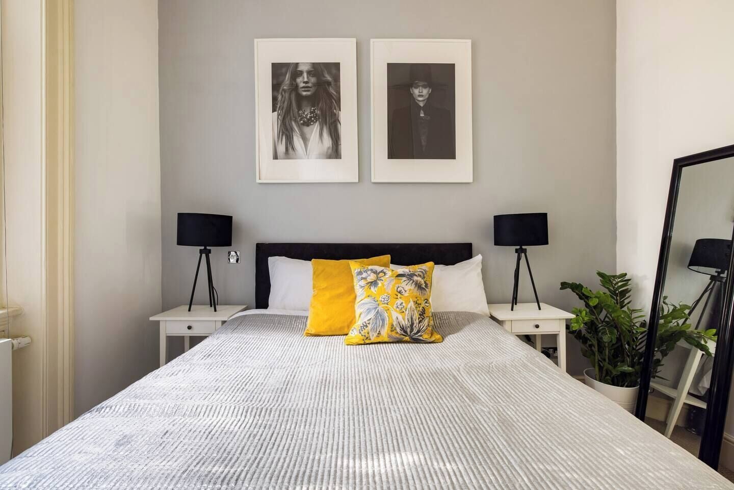 Un dormitorio ordenado con una cama grande, dos mesitas de noche, dos lámparas negras y dos cuadros en la pared.