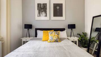 Un dormitorio ordenado con una cama grande, dos mesitas de noche, dos lámparas negras y dos cuadros en la pared.