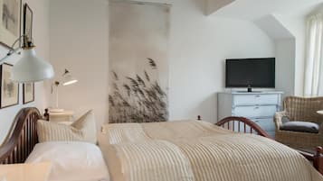 Un dormitorio con cama, televisor, cómoda y una silla de mimbre.