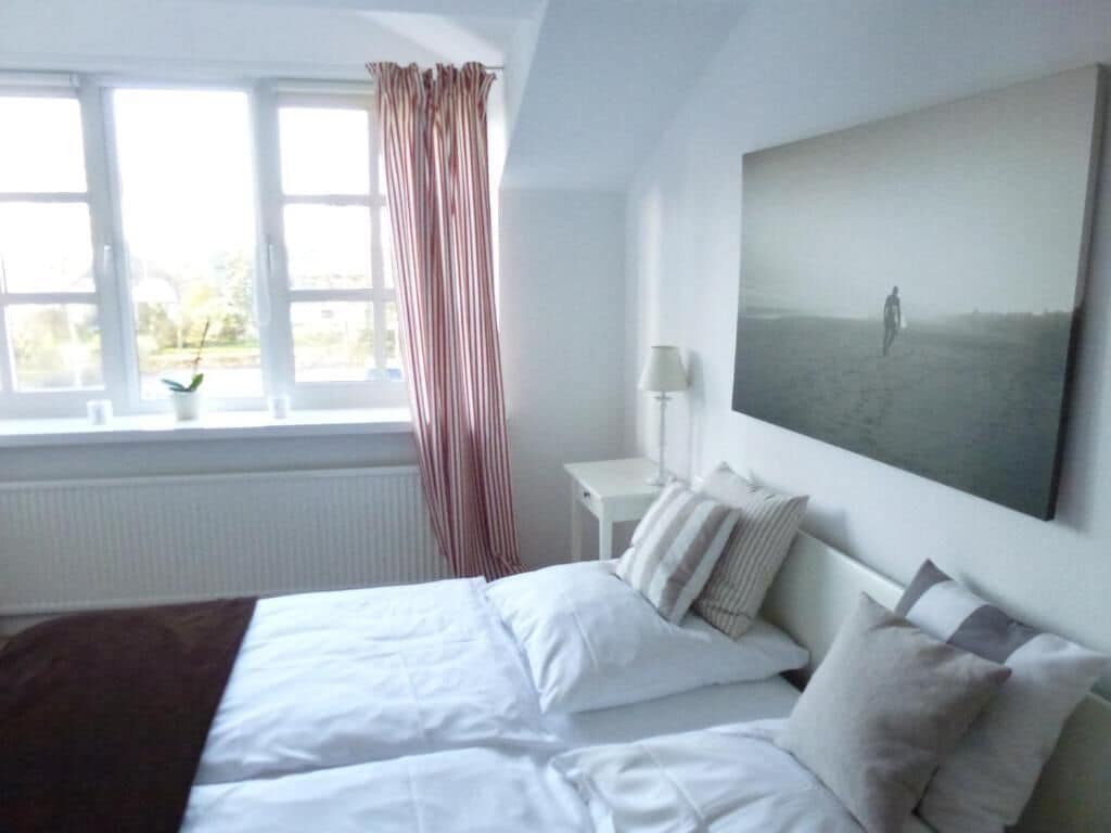 A bedroom with a bed, a window with curtains, a bedside table with a lamp, and a large painting on the wall.