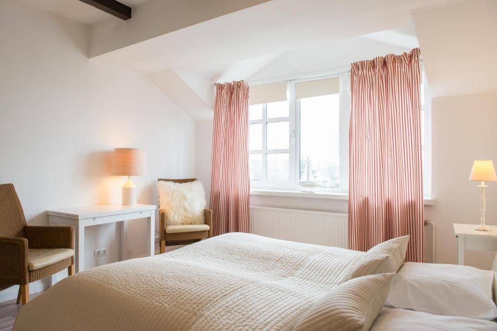 Una habitación de hotel con cama, escritorio, silla y ventana con cortinas.