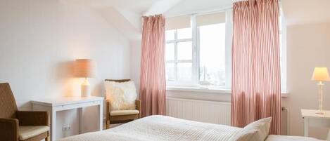 Una habitación de hotel con cama, escritorio, silla y ventana con cortinas.