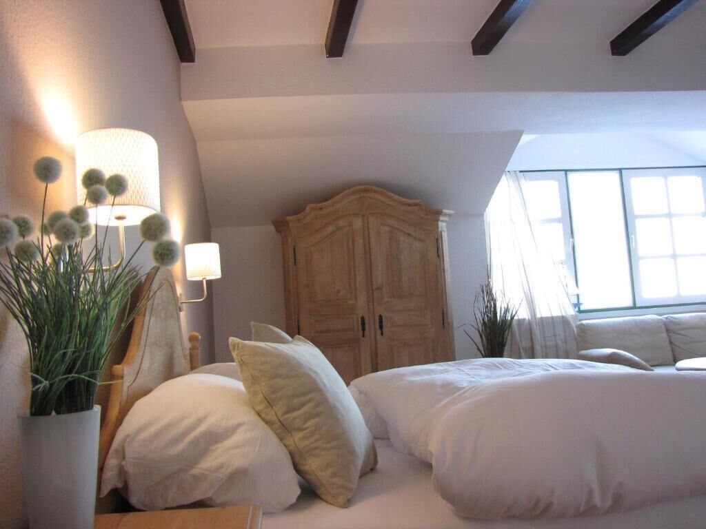 Une chambre avec une grande armoire, un lit avec une literie blanche et une plante en pot.