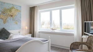 A bedroom with a bed, a map on the wall, a window with curtains, a TV, and a chair. - Strandhotel Lodge am Meer (Gluecksburg)