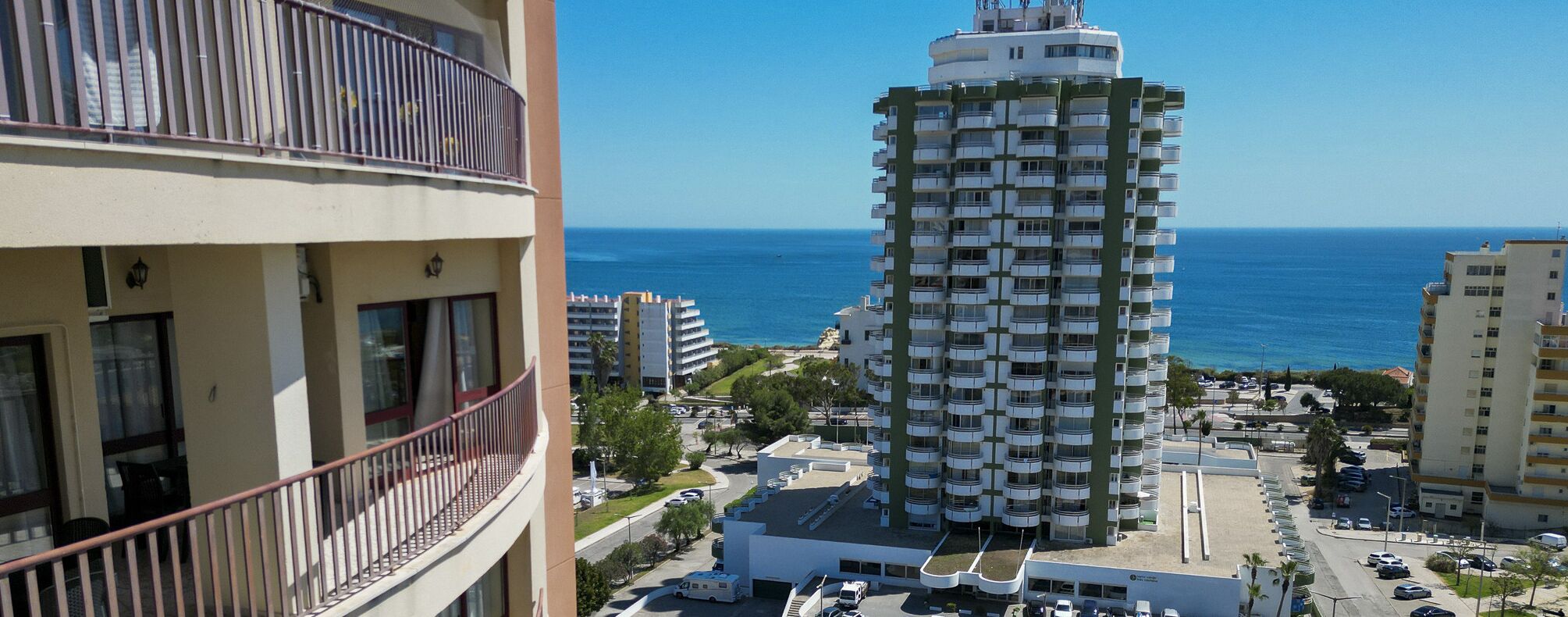 A high-rise building with multiple balconies, a parking area, and a view of the sea.