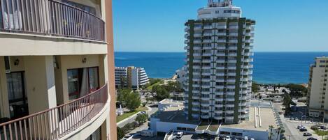 A high-rise building with multiple balconies, a parking area, and a view of the sea.