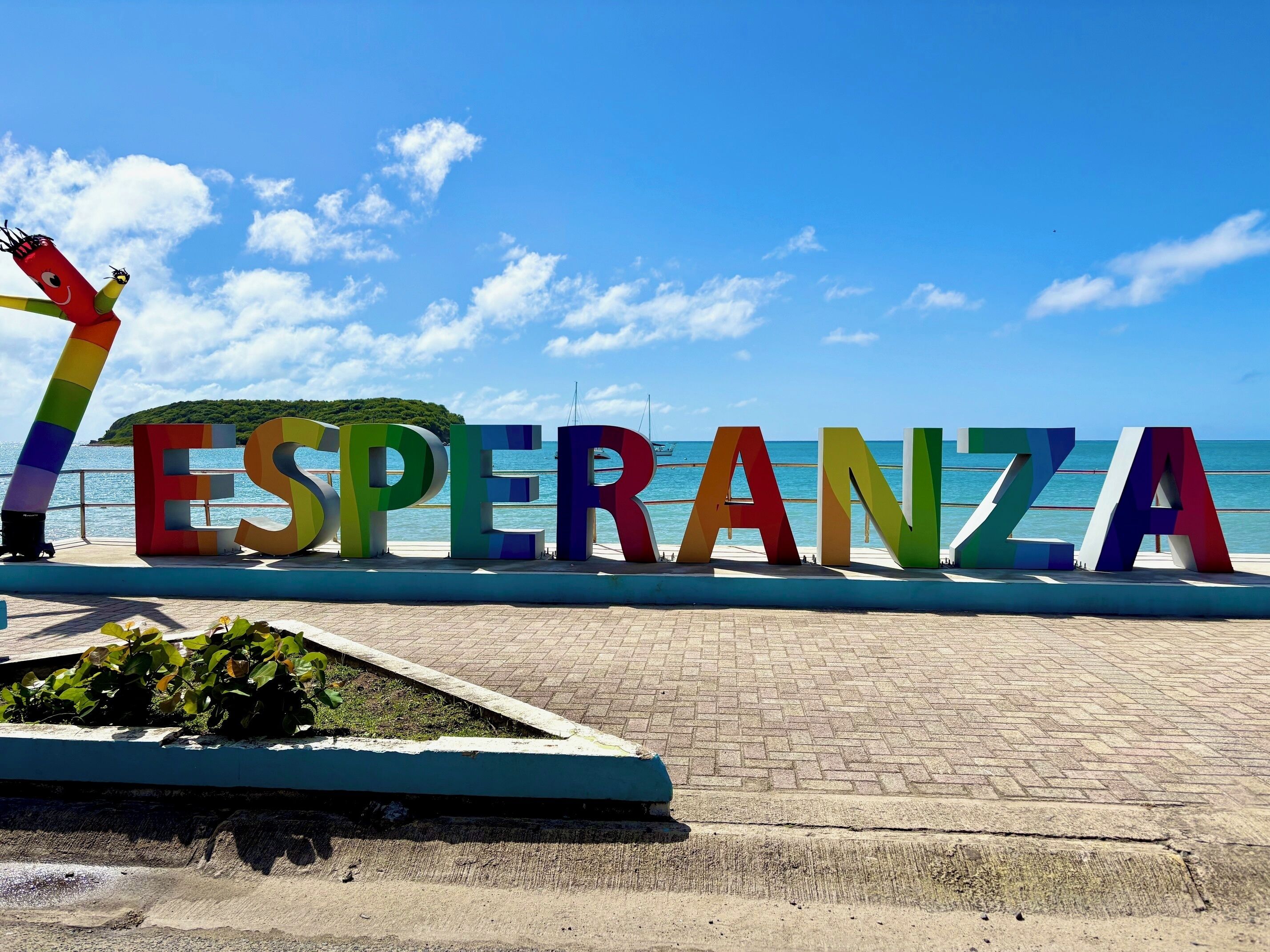 Ein farbiges Schild mit der Aufschrift "ESPERANZA", links davon eine stange in Regenbogenfarben.