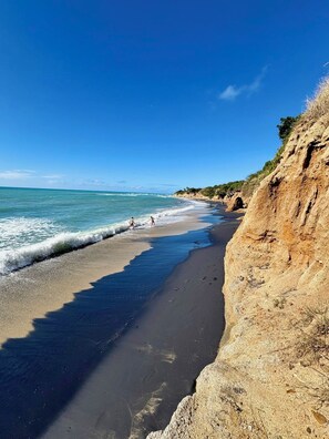 Una playa con aguas azules cristalinas, una orilla de arena y un acantilado rocoso.