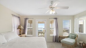 Une chambre avec un grand lit, un ventilateur de plafond et une vue sur l’extérieur, visible à travers une porte.