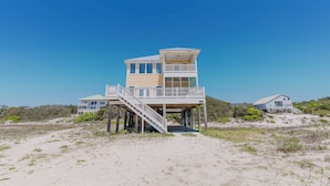 Une maison située en bord de mer, dotée d’un balcon et d’un escalier menant à l’entrée principale.