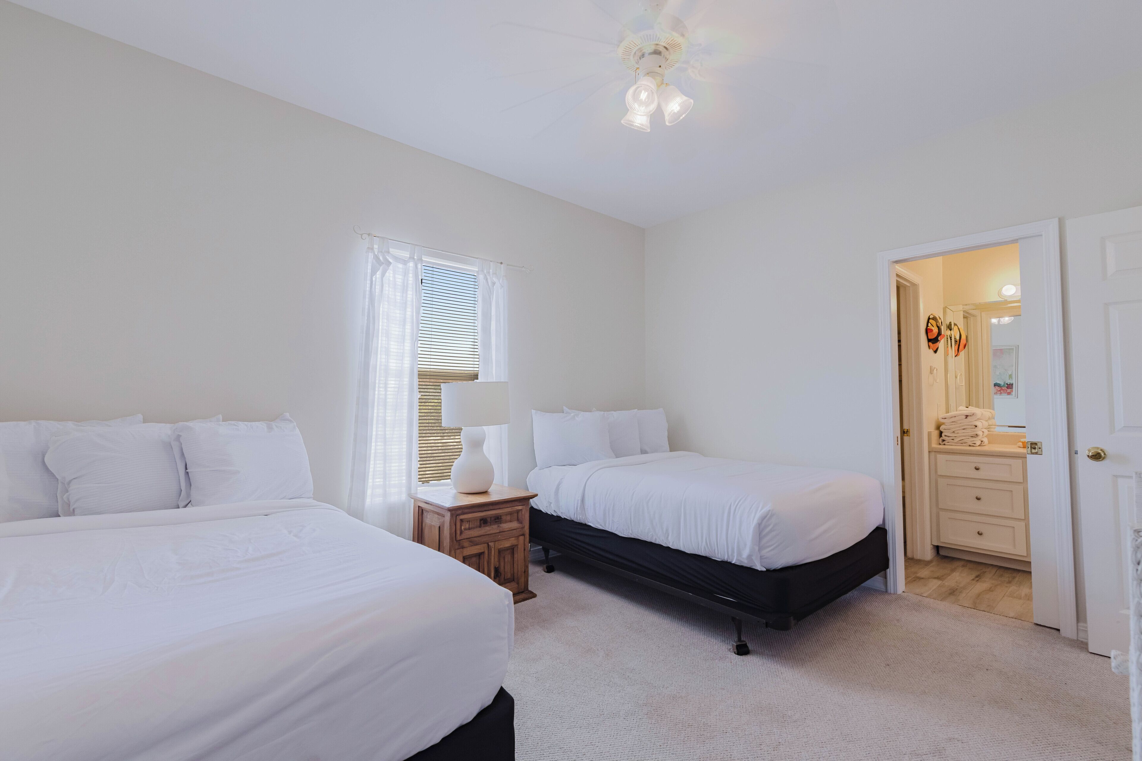 A bedroom with two beds, a nightstand, a lamp, and a door leading to a bathroom.