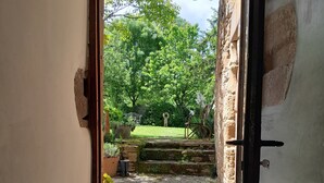 A doorway leading to a garden with a stone pathway, a chair, and a potted plant. - Large medieval village house, pets welcome, private pool. (Salles)