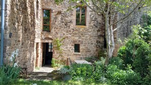 A rustic stone building with a small garden, a wooden door, and a tree providing shade. - Large medieval village house, pets welcome, private pool. (Salles)