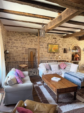 A rustic room with exposed wooden beams, a stone wall, a sofa, a coffee table, and a bookshelf. - Large medieval village house, pets welcome, private pool. (Salles)