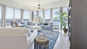 A spacious living room with a large window, a ceiling fan, and a view of the city. - Caribe Resort 107B by Liquid Life (Orange Beach)