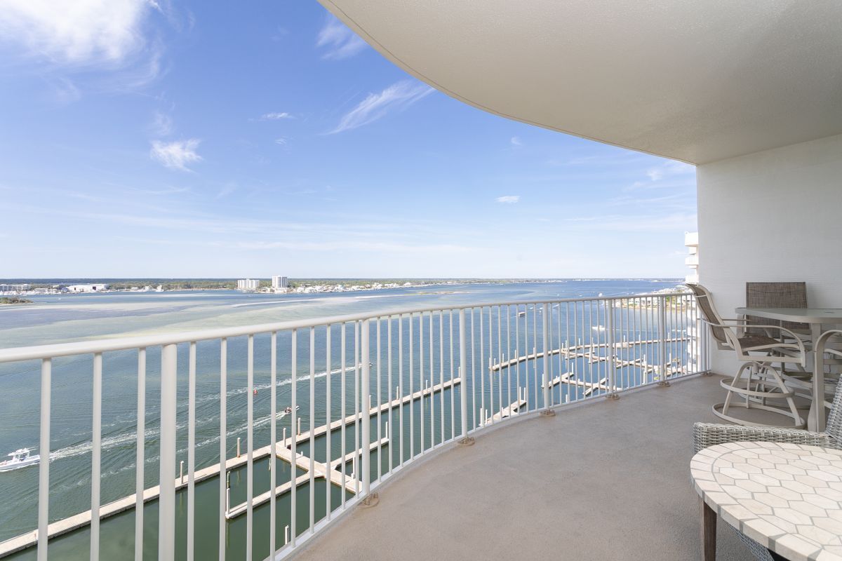 A balcony with a view of the sea and a marina. There is a table and chairs on the balcony.