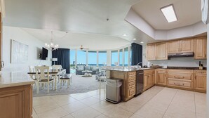 Una cocina amplia con armarios de madera, una isla central y vistas al exterior. Hay un comedor con mesa y sillas, y una sala de estar con sofá y televisor.