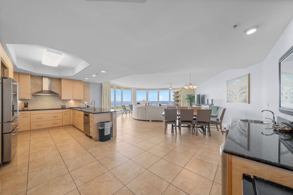 A modern kitchen with a central island, a dining area with chairs, and a large window offering a view.