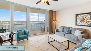 Amplia sala de estar con balcón, ventilador de techo y ventana grande con vistas al agua.