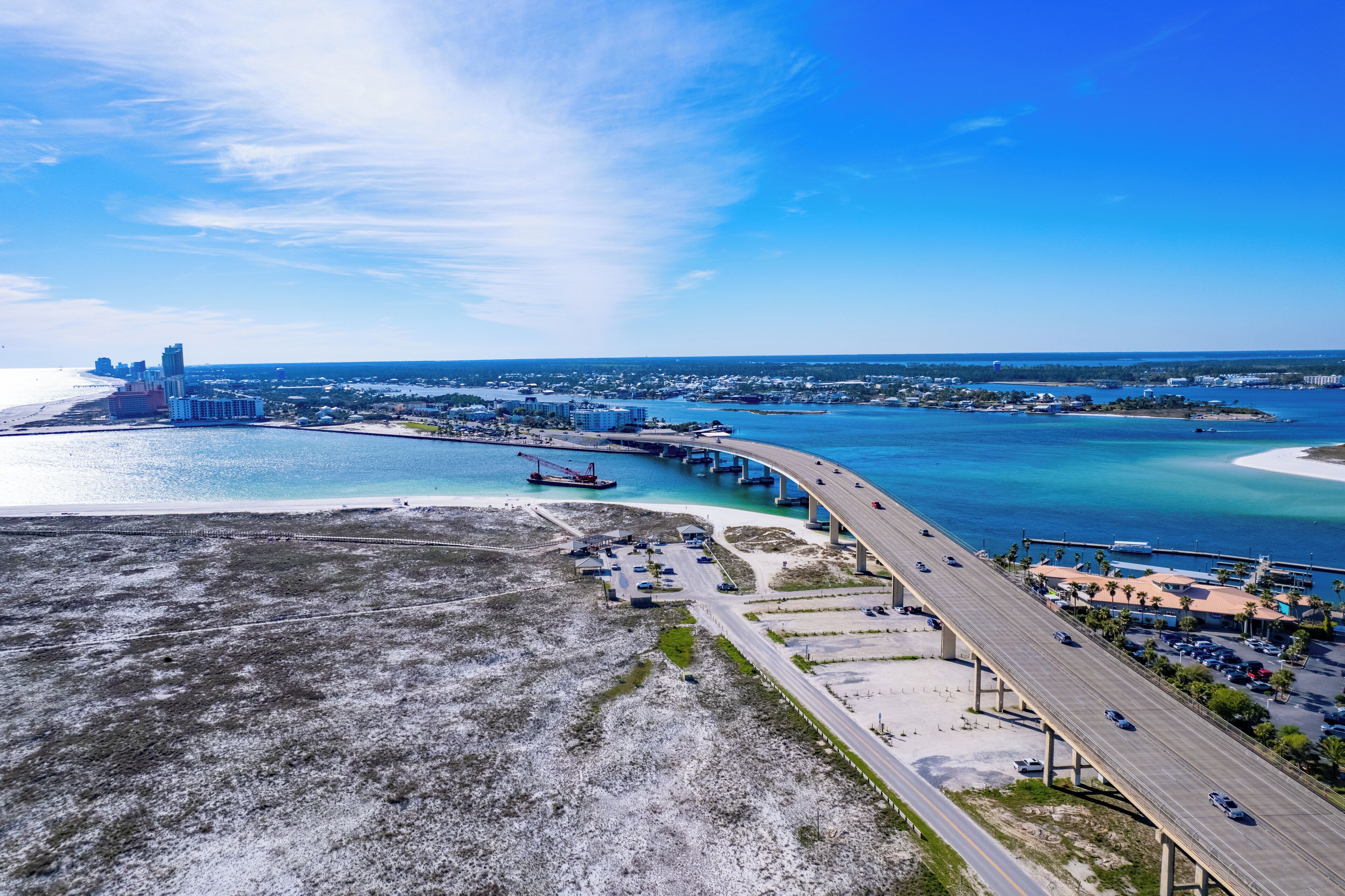 Une vue aérienne d’une ville côtière, avec un pont imposant, des eaux d’un bleu limpide et un mélange de paysages urbains et naturels.