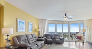 A living room with a sofa, armchair, and a table with a lamp. There are two framed pictures on the wall.