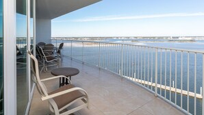 A balcony with a view of the water, chairs, and a table.