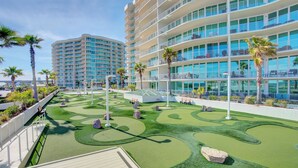 A resort with a golf course, a large building with balconies, and palm trees. - Caribe Resort 215D by Liquid Life (Orange Beach)