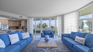 A modern living room with blue sofas and a wooden coffee table, a kitchen in the background, and a balcony with a view. - Caribe Resort 215D by Liquid Life (Orange Beach)