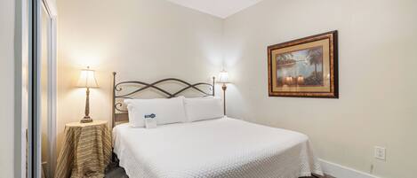 A neatly arranged bedroom with a bed, two bedside lamps, a small table with a lamp, and a framed picture on the wall.