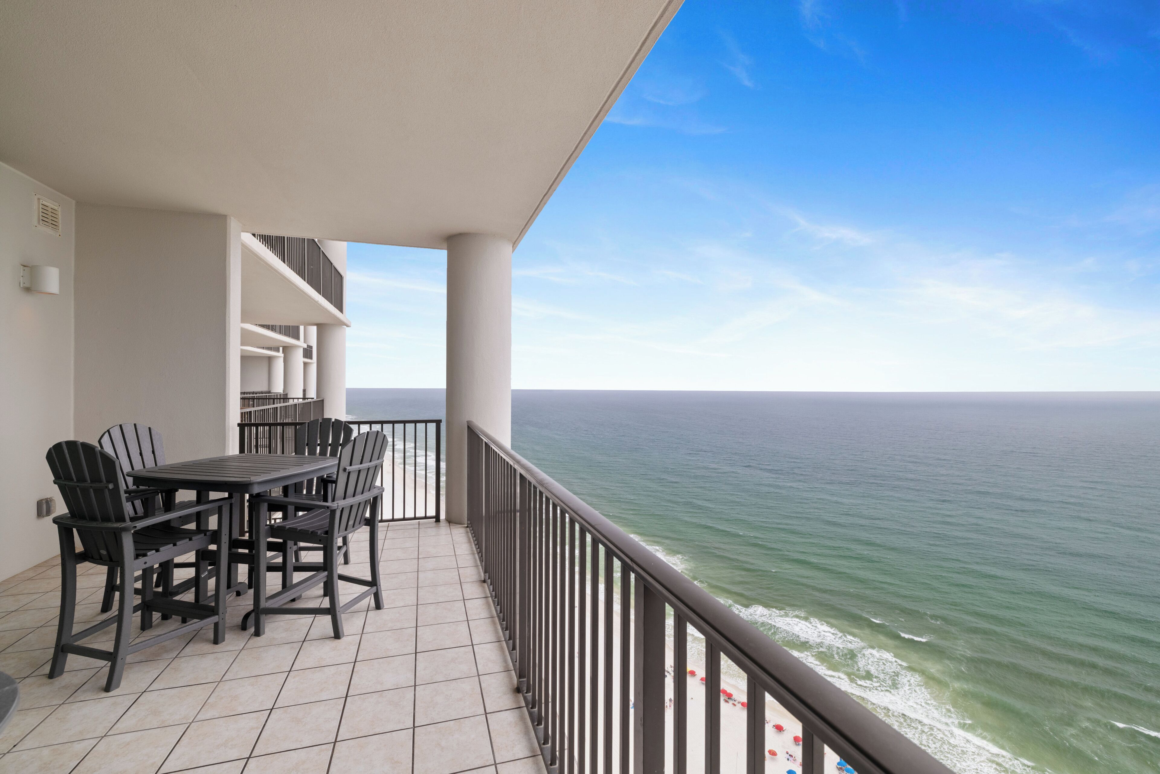 A balcony with a view of the ocean, a table with chairs, and a railing.